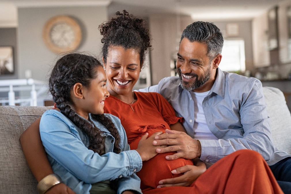 Pregnant woman with daughter and partner sitting on sofa