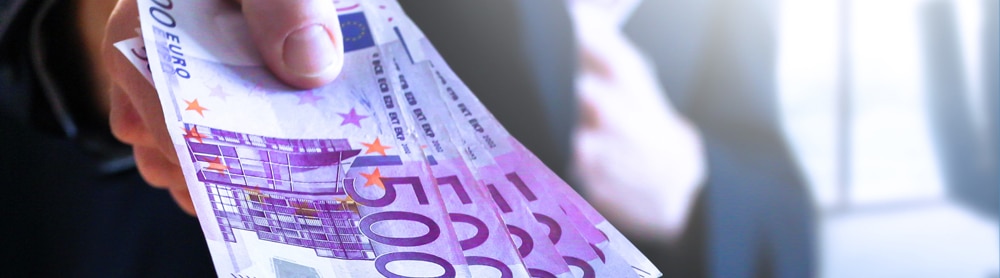 Mann zeigt viel Geld in die Kamera und steckt sich weiteres Geld in Jackentasche