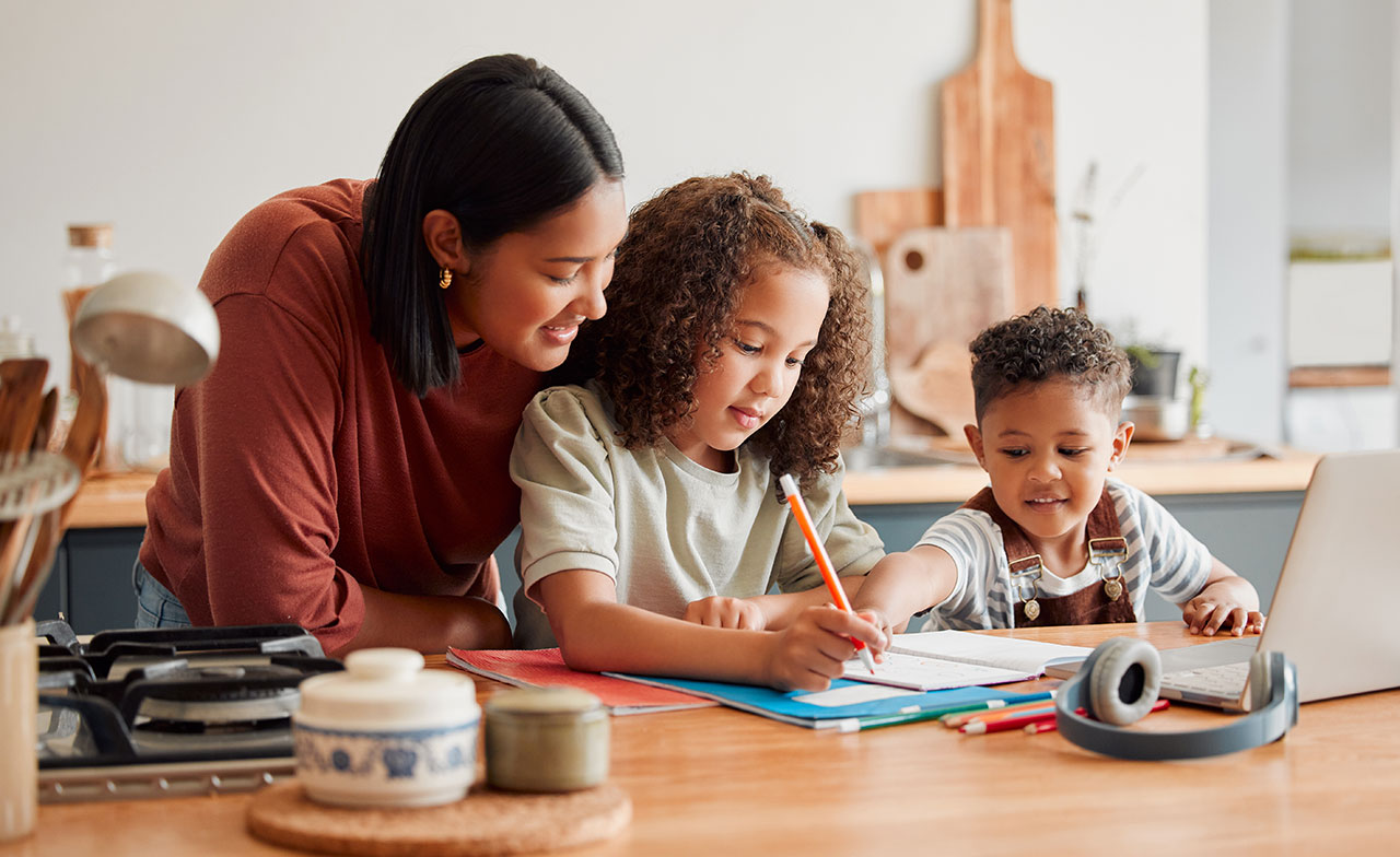 En mamma hjälper sina barn med läxorna vid köksbordet.