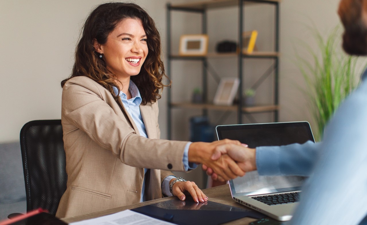 Two professionals smiling and shaking hands across a desk
