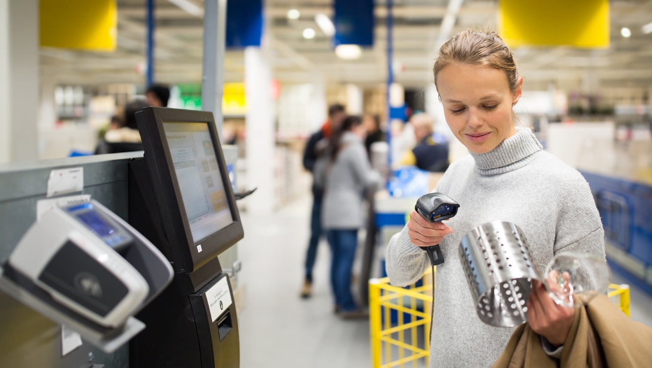 Frau scannt an einer Selbstbedienungskasse ihre Ware