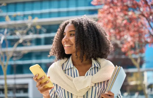 Person holding mobile phone standing in front of building and trees