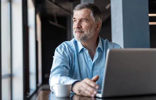 Mann sitzt vor seinem Laptop und schaut in die Ferne
