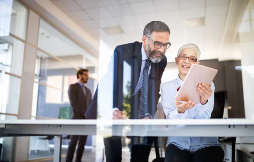 Zwei Kollegen in einer Bank freuen sich über den erfolgreichen KI-gestützten Onboarding-Prozess…