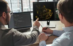 two AI experts looking at models on computer monitor