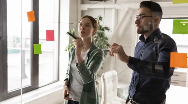 Zwei Berater stehten vor einer Glaswand mit Postit