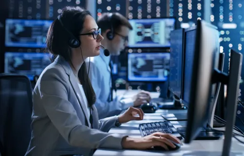 Two people with headsets sit in a control centre