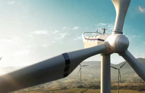man stands on a wind turbine with more turbines in the landscape in the background