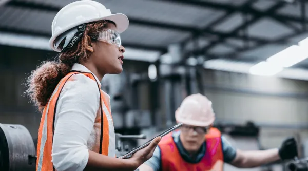 Two individuals wearing safety vests and hard hats in an industrial setting