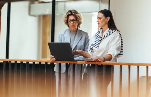 Zwei Verwaltungsfachangestellte stehen mit einem Laptop in einem Büroflur