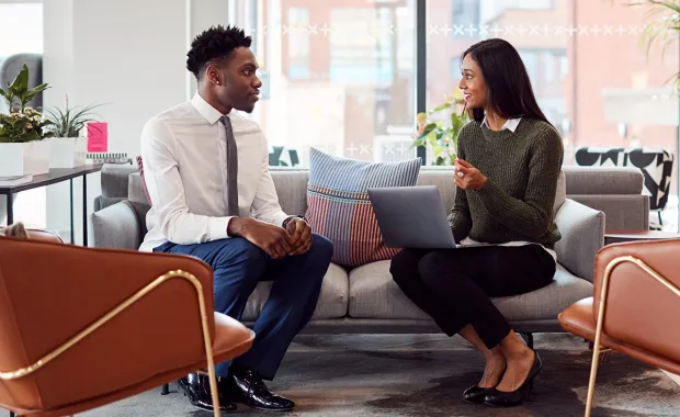two people sit on sofa chatting over a laptop