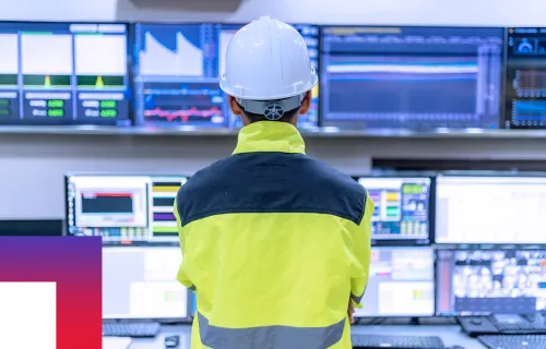 A utilities worker in hardhat looking at data in a computer control center