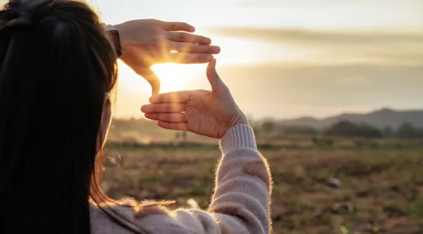 Ilmiön ytimessä hero banner. Image: woman looking at the sun through her hands.